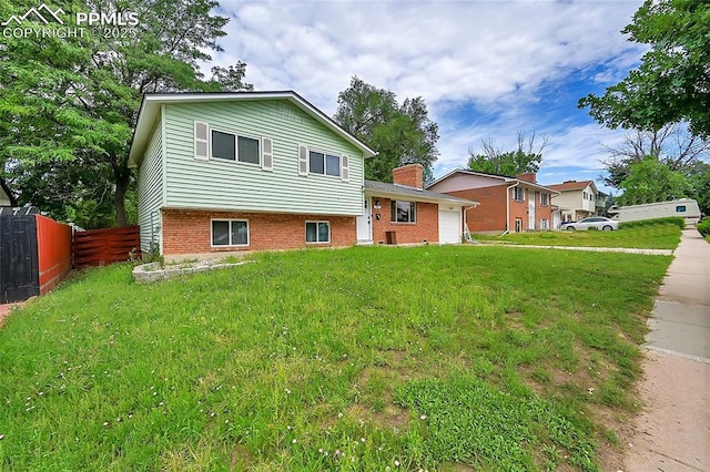 tri-level home with fence, a chimney, a garage, a front yard, and brick siding