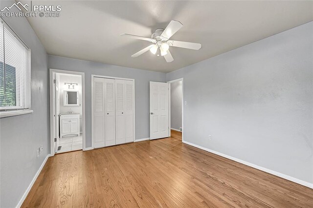 unfurnished bedroom featuring a closet, baseboards, ceiling fan, light wood-style floors, and ensuite bath