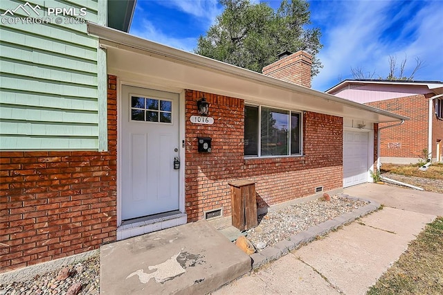 entrance to property with concrete driveway, a chimney, brick siding, crawl space, and a garage