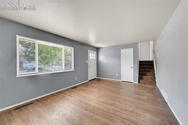 unfurnished living room featuring baseboards, visible vents, wood finished floors, and stairway