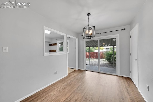 unfurnished dining area with baseboards, wood finished floors, and a chandelier