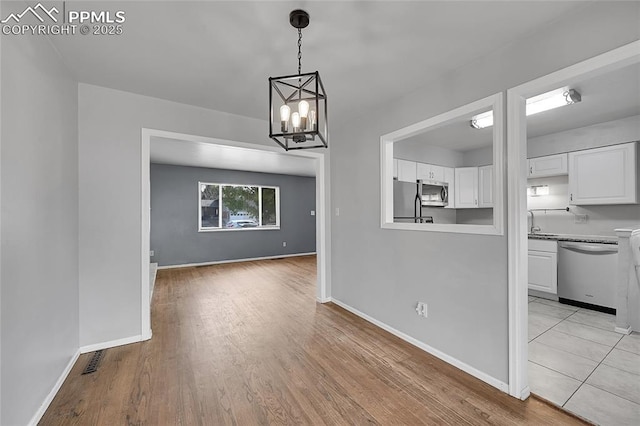 unfurnished dining area featuring baseboards, light wood-style floors, and an inviting chandelier