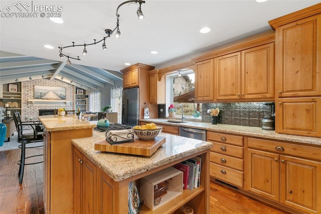 kitchen with wood finished floors, a kitchen island, appliances with stainless steel finishes, a sink, and vaulted ceiling with beams