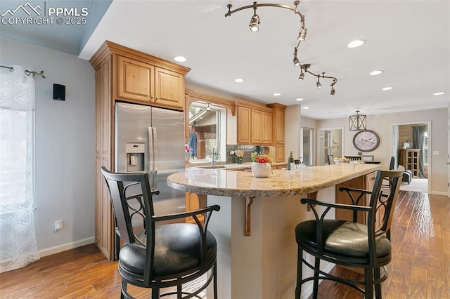kitchen with a kitchen breakfast bar, decorative backsplash, light stone countertops, and wood finished floors