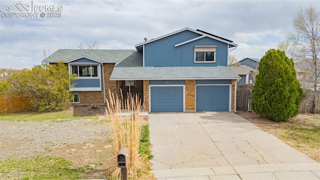 7775 Woody Creek Dr, Colorado Springs, CO 80911 - split level home with concrete driveway, roof with shingles, fence, an attached garage, and brick siding