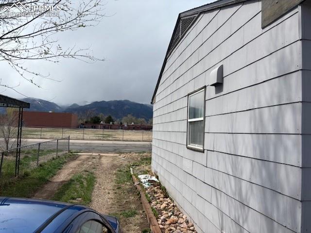 view of side of home with fence, a rural view, and a mountain view