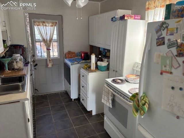 kitchen featuring white cabinets, light countertops, white appliances, dark tile patterned flooring, and a sink