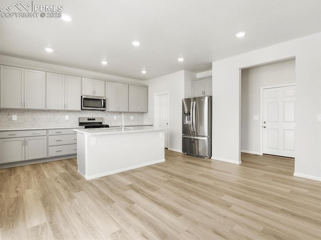 kitchen featuring stainless steel appliances, light countertops, gray cabinets, light wood-style floors, and decorative backsplash
