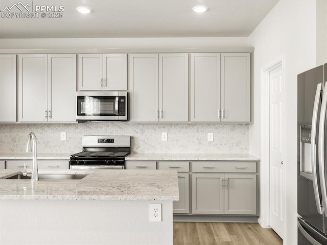 kitchen with a sink, light wood-style floors, gray cabinets, appliances with stainless steel finishes, and light stone countertops