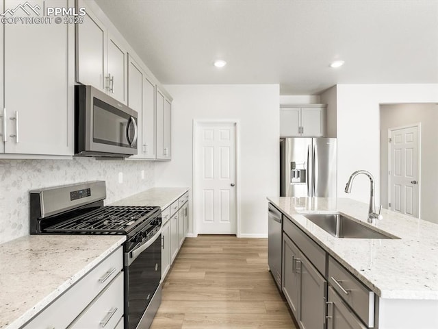 kitchen with a sink, decorative backsplash, a center island with sink, light wood-style flooring, and appliances with stainless steel finishes