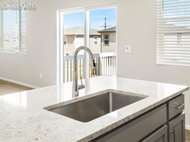 kitchen featuring light stone counters, gray cabinets, a sink, a wealth of natural light, and baseboards