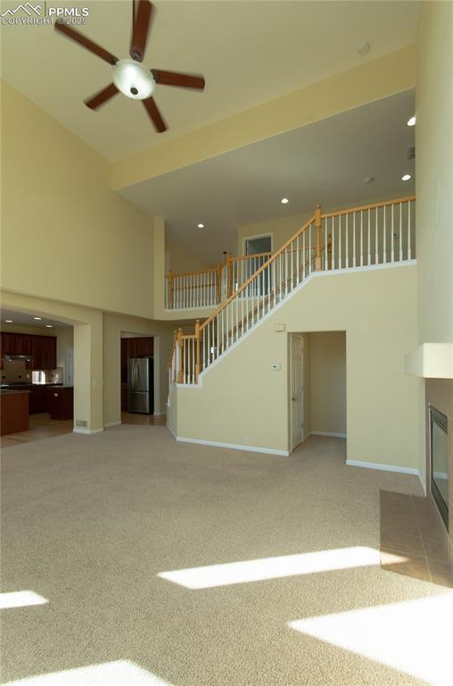 9443 St George Rd, Peyton, CO 80831 - unfurnished living room featuring light carpet, a tiled fireplace, stairway, a high ceiling, and ceiling fan