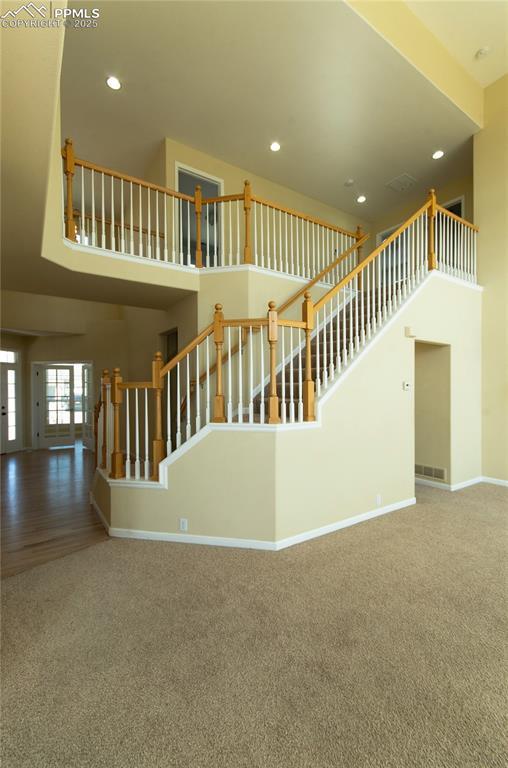 9443 St George Rd, Peyton, CO 80831 - unfurnished living room with a towering ceiling, carpet floors, recessed lighting, stairs, and baseboards