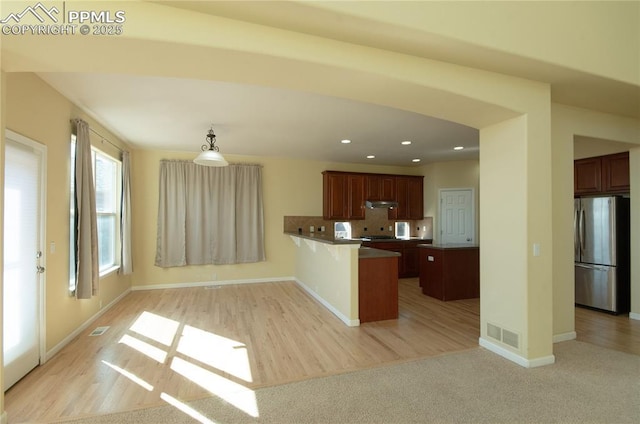 9443 St George Rd, Peyton, CO 80831 - kitchen featuring freestanding refrigerator, a peninsula, a breakfast bar, under cabinet range hood, and decorative backsplash