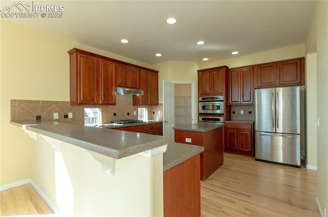 9443 St George Rd, Peyton, CO 80831 - kitchen featuring light wood-style flooring, tasteful backsplash, a center island, appliances with stainless steel finishes, and under cabinet range hood