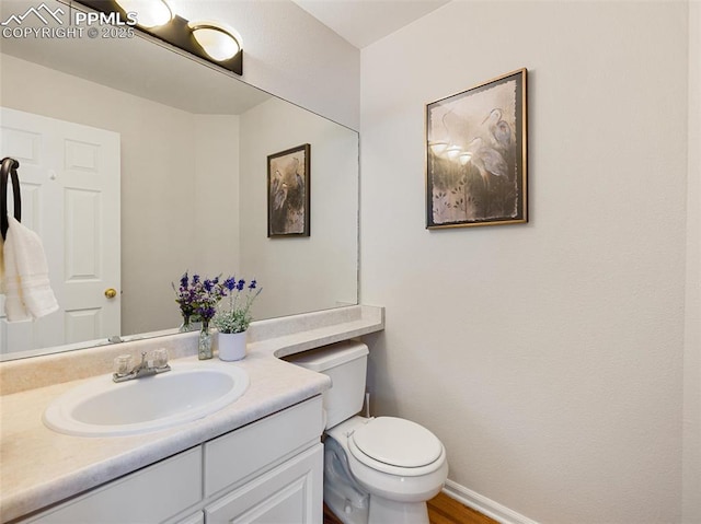 half bathroom featuring vanity, baseboards, toilet, and wood finished floors