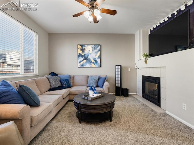 living area with a tiled fireplace, baseboards, a ceiling fan, and carpet floors