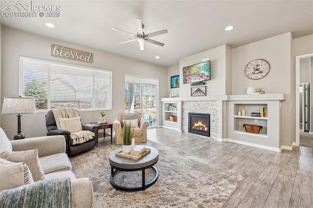 living room with ceiling fan, wood finished floors, recessed lighting, and a stone fireplace