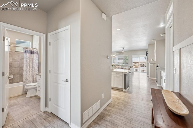 corridor featuring visible vents, baseboards, light wood finished floors, and a textured ceiling