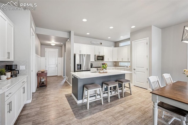 kitchen with a sink, white cabinetry, a breakfast bar, appliances with stainless steel finishes, and light wood-style floors