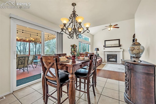 dining room featuring lofted ceiling, visible vents, light tile patterned floors, a tiled fireplace, and ceiling fan with notable chandelier