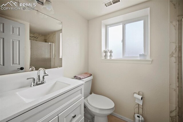 bathroom with toilet, vanity, an enclosed shower, and visible vents