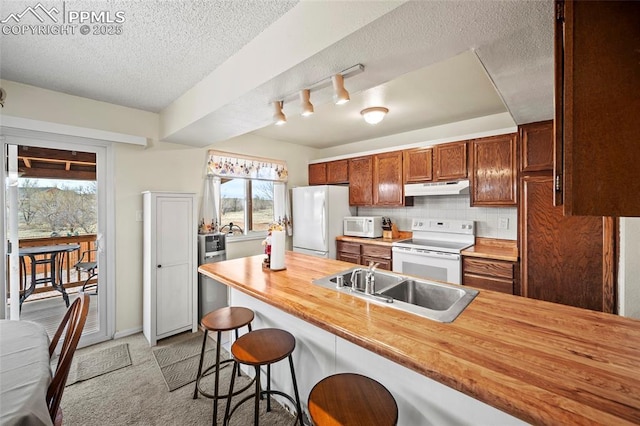 kitchen with white appliances, under cabinet range hood, a breakfast bar, a sink, and wood counters