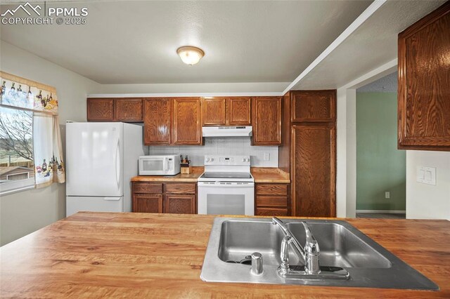 kitchen featuring white appliances, wood counters, under cabinet range hood, and backsplash