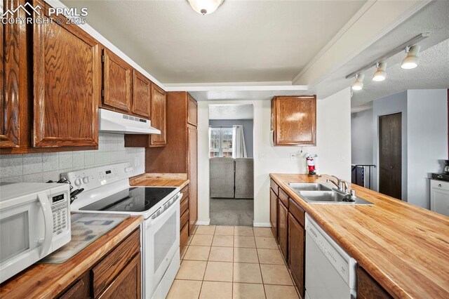 kitchen featuring white appliances, under cabinet range hood, decorative backsplash, a sink, and light tile patterned flooring