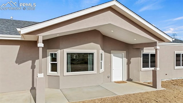 view of exterior entry featuring a patio area, a shingled roof, and stucco siding