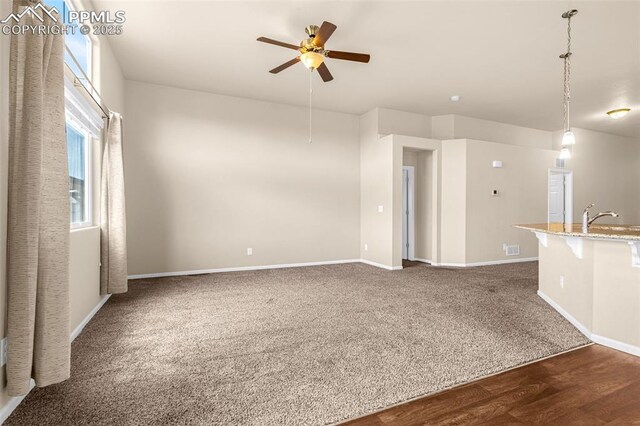 9712 Wando Dr, Colorado Springs, CO 80925 - unfurnished living room featuring baseboards, ceiling fan, dark wood-type flooring, dark carpet, and a sink