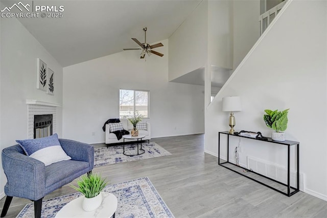 living room featuring wood finished floors, high vaulted ceiling, a ceiling fan, and a brick fireplace
