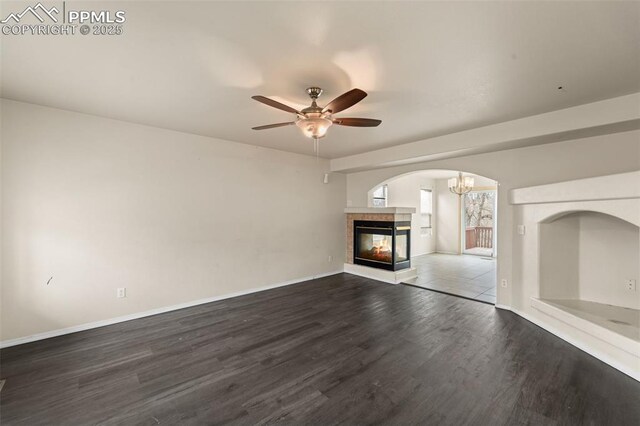 795 Ridgebury Pl, Fountain, CO 80817 - unfurnished living room with baseboards, arched walkways, a multi sided fireplace, wood finished floors, and ceiling fan with notable chandelier
