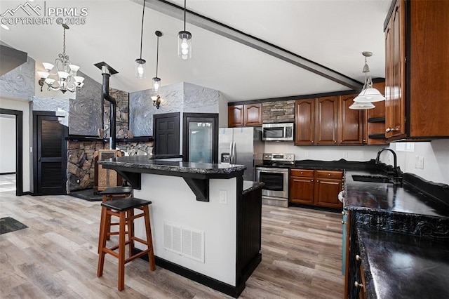 kitchen featuring a kitchen island, visible vents, appliances with stainless steel finishes, a wood stove, and a sink