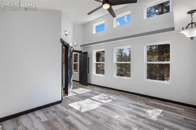 unfurnished living room with a towering ceiling, wood finished floors, baseboards, ceiling fan, and a barn door
