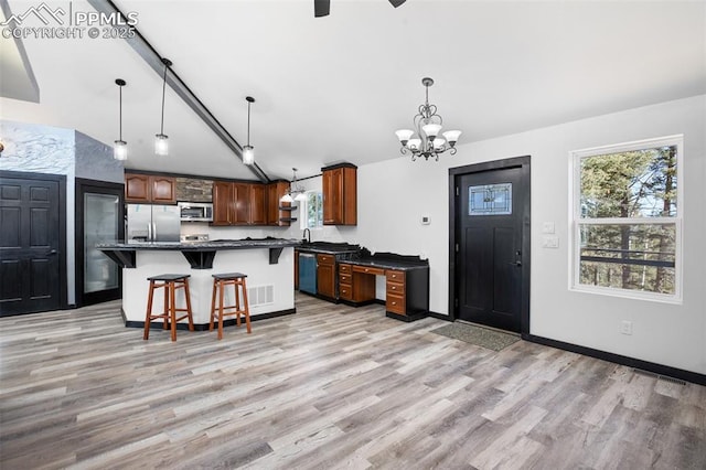 kitchen featuring dark countertops, a breakfast bar, a notable chandelier, light wood-style flooring, and stainless steel appliances