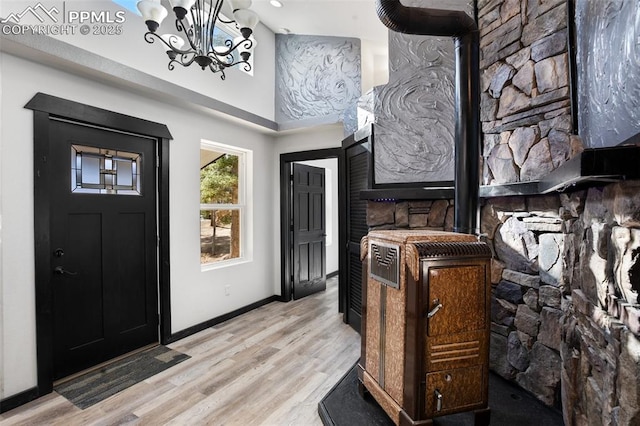 entryway featuring an inviting chandelier, a wood stove, light wood finished floors, baseboards, and a towering ceiling