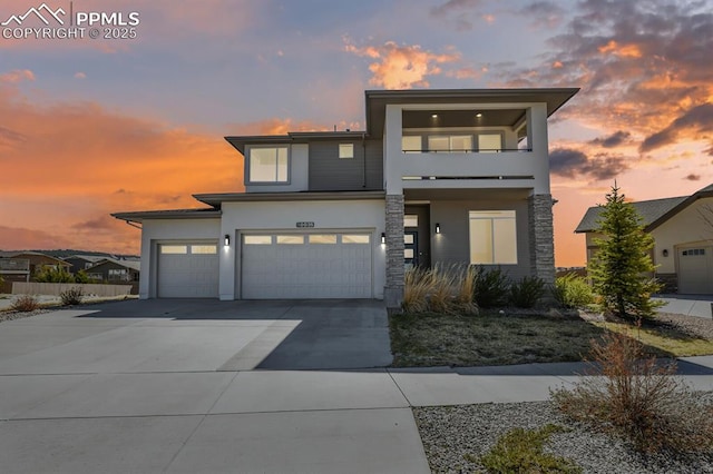 contemporary house with stucco siding, a garage, driveway, stone siding, and a balcony