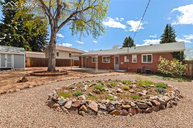 2928 Drakestone Dr, Colorado Springs, CO 80909 - back of house featuring a storage unit, brick siding, a fenced backyard, an outbuilding, and a patio area