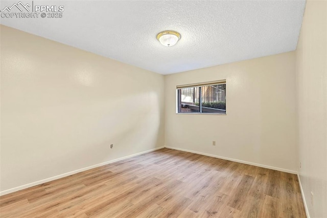 empty room with baseboards, light wood-type flooring, and a textured ceiling