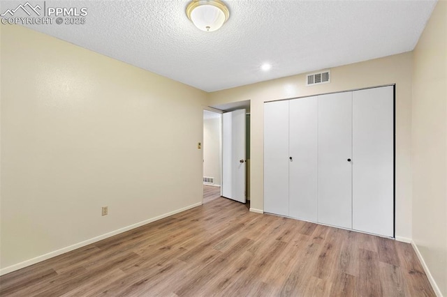 unfurnished bedroom with a closet, light wood-type flooring, baseboards, a textured ceiling, and visible vents