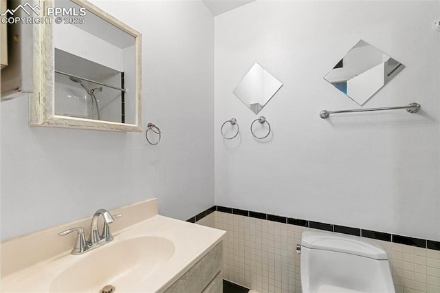 bathroom featuring toilet, vanity, a wainscoted wall, and tile walls