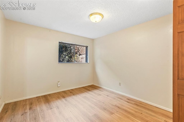 spare room featuring a textured ceiling, light wood finished floors, and baseboards