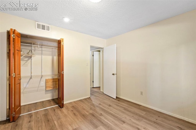 unfurnished bedroom with a closet, baseboards, a textured ceiling, visible vents, and wood finished floors