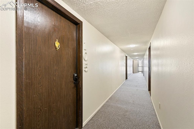 hallway featuring carpet flooring, a textured ceiling, and baseboards