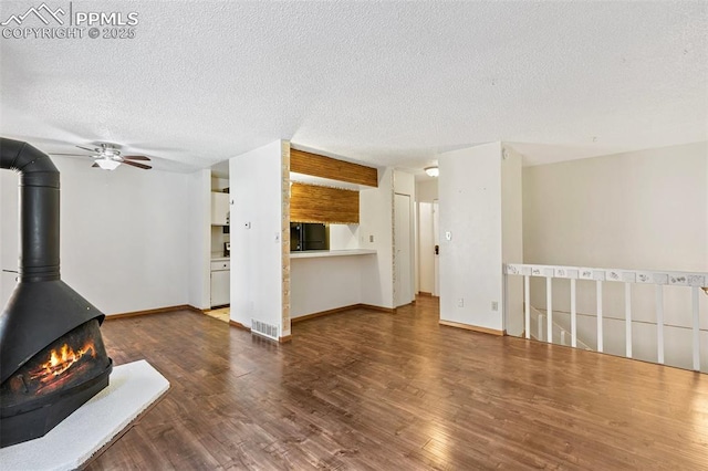 unfurnished living room featuring a textured ceiling, wood finished floors, a ceiling fan, and visible vents