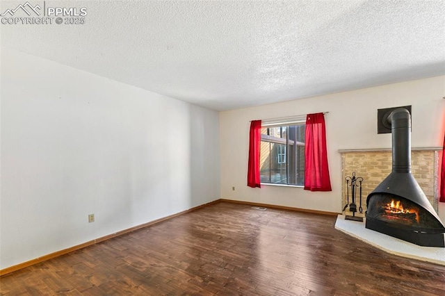 unfurnished living room featuring a wood stove, baseboards, a textured ceiling, and wood finished floors