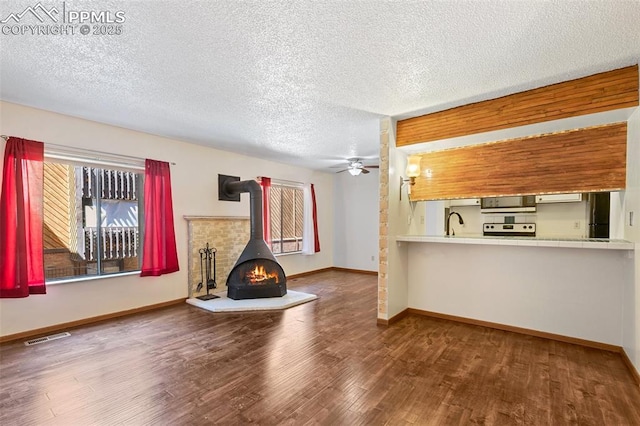 unfurnished living room featuring visible vents, a wood stove, a ceiling fan, a textured ceiling, and wood finished floors