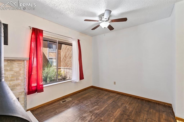 unfurnished room with baseboards, a ceiling fan, a wood stove, visible vents, and wood finished floors