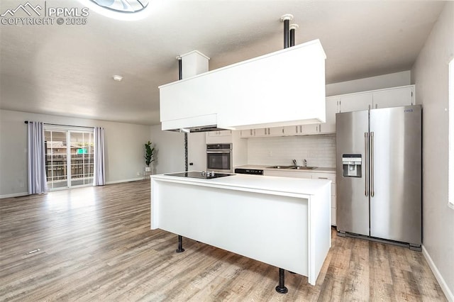 kitchen with stainless steel appliances, a sink, light wood finished floors, light countertops, and tasteful backsplash